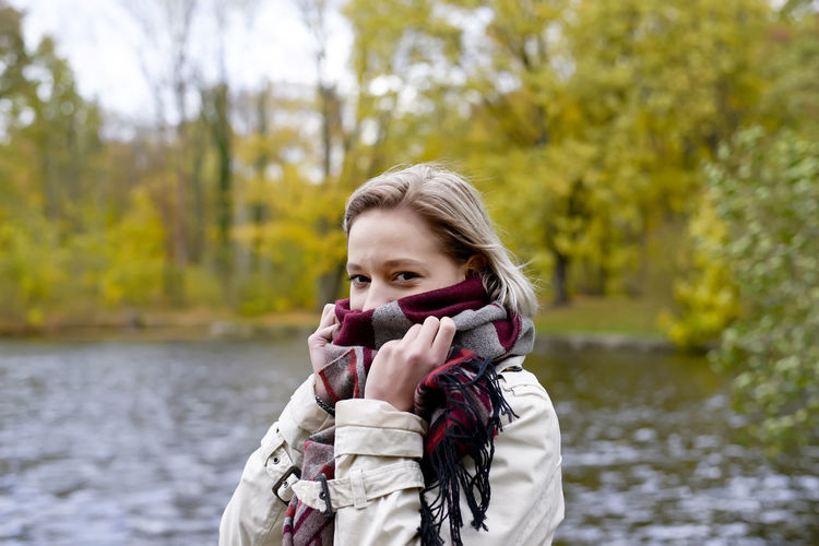 Portrait of young woman with covering face with scarf standing against lake