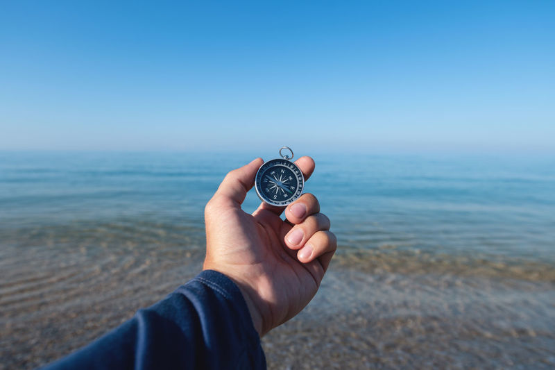Compass in a man's hand against the background of the morning sea and pebble beach. travel by sea