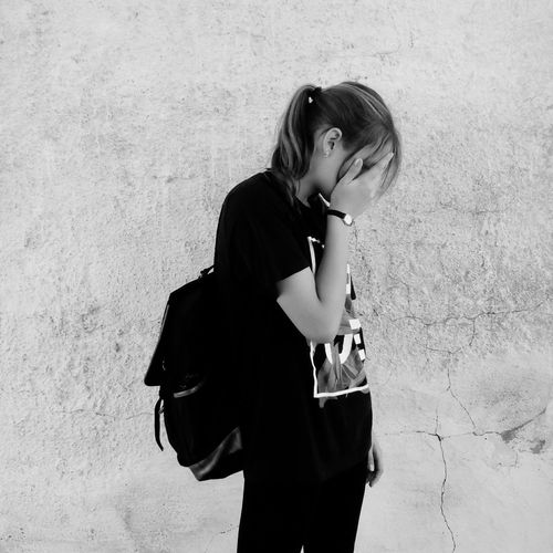 Young woman covering face while standing against wall