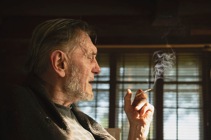 Close-up of a smoking senior man looking through window