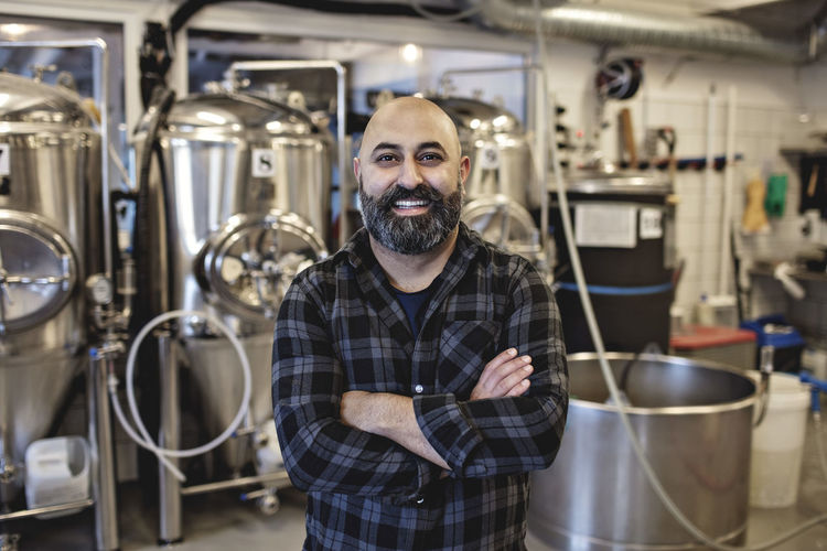 Portrait of smiling manager standing with arms crossed at brewery