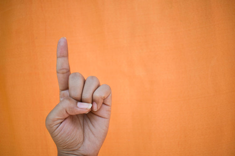Close-up of man holding hands against orange background