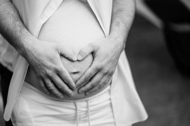 Cropped hands of man toughing pregnant wife stomach outdoors