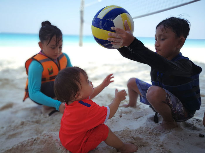 Boy with sisters holding volleyball at beach