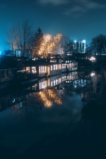 Illuminated city by lake against sky at night
