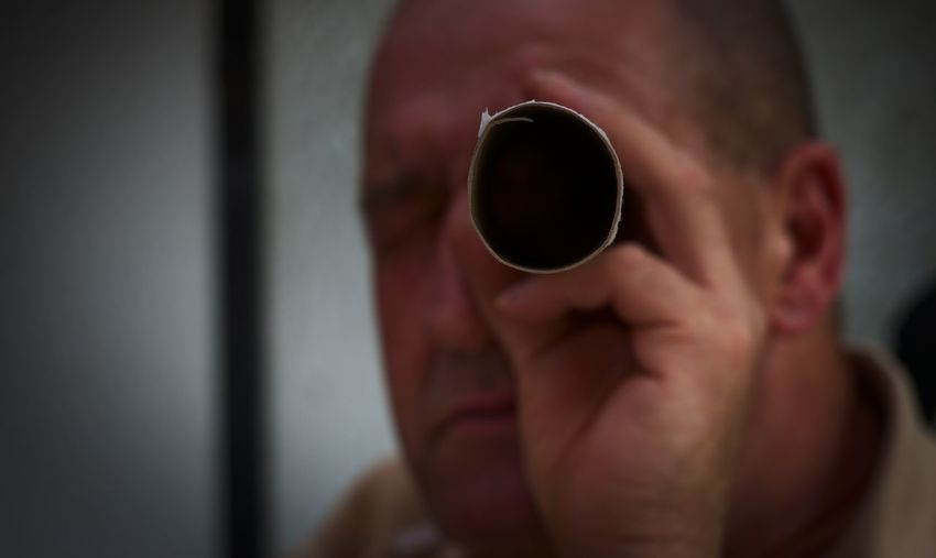 Close-up of man looking through paper roll