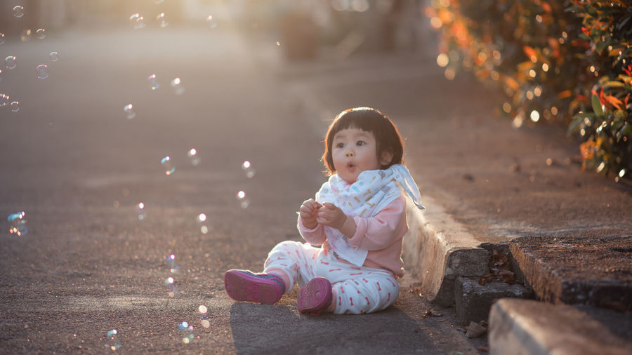 Cute girl looking at bubbles while sitting on road