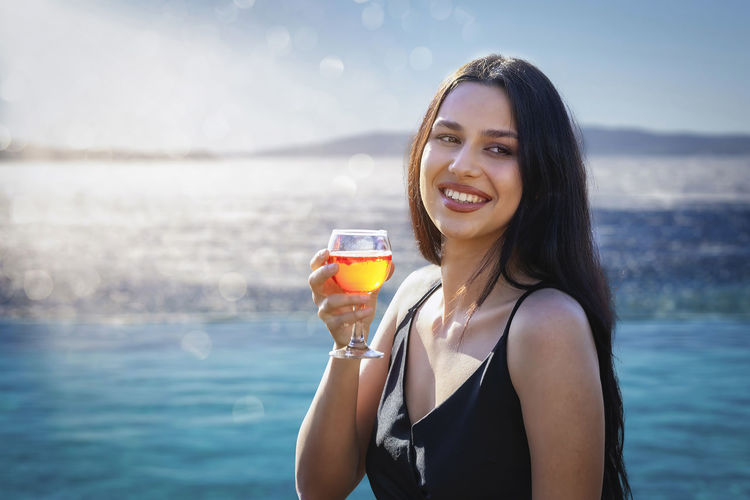 Smiling woman holding drink against sea