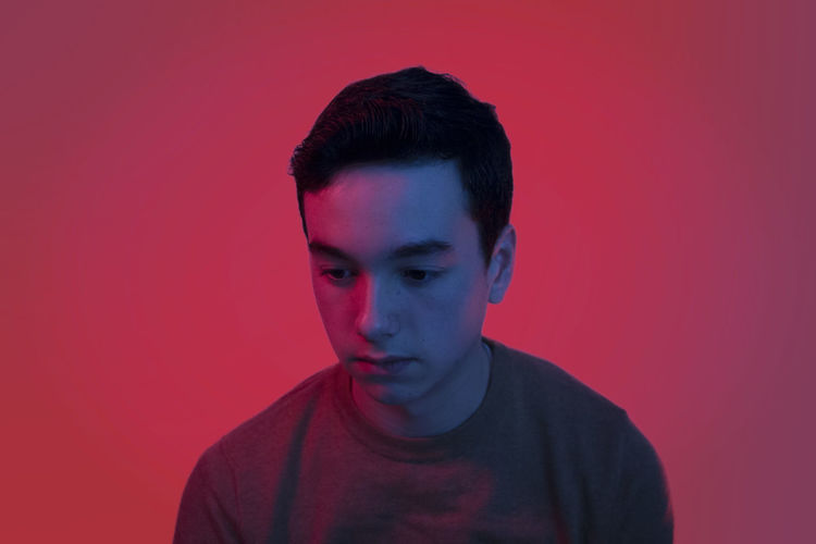Thoughtful teenage boy looking down against red background