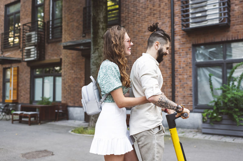 Happy couple riding electric push scooter on street in city