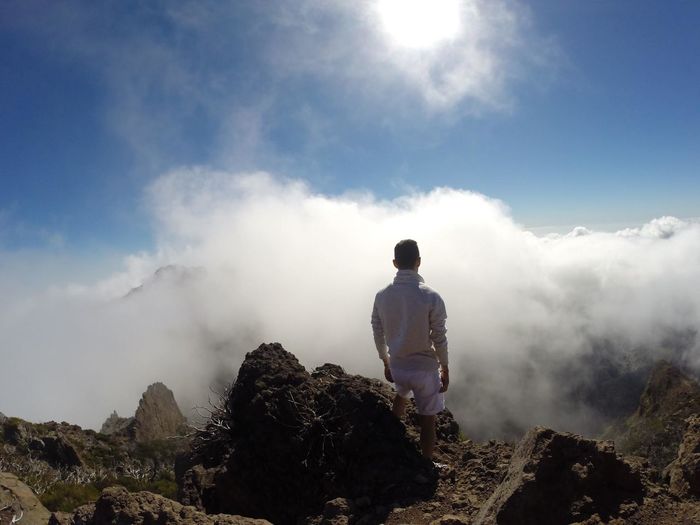 Rear view of man standing on mountain against cloudy sky