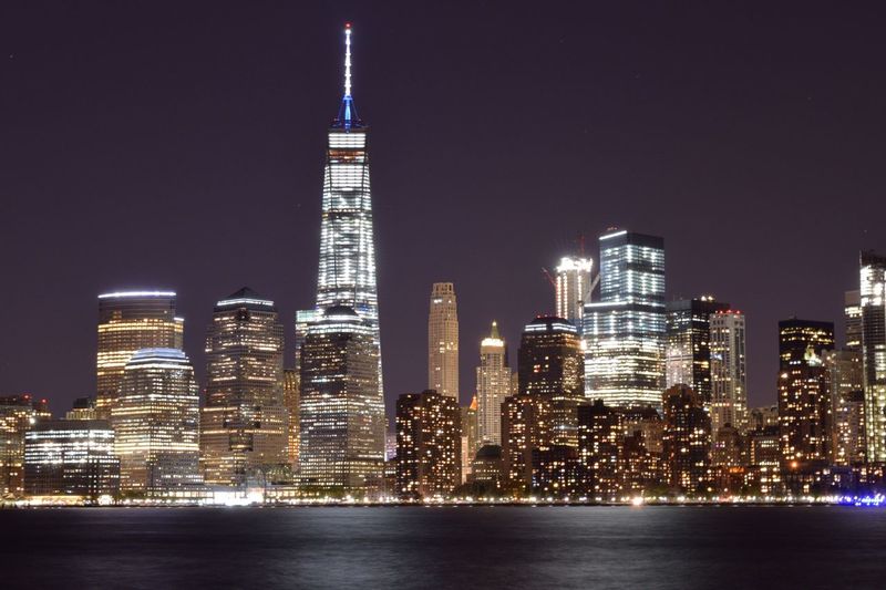 Illuminated buildings by river against clear sky at night