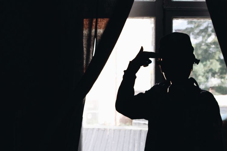 Silhouette boy gesturing shooting his head at home