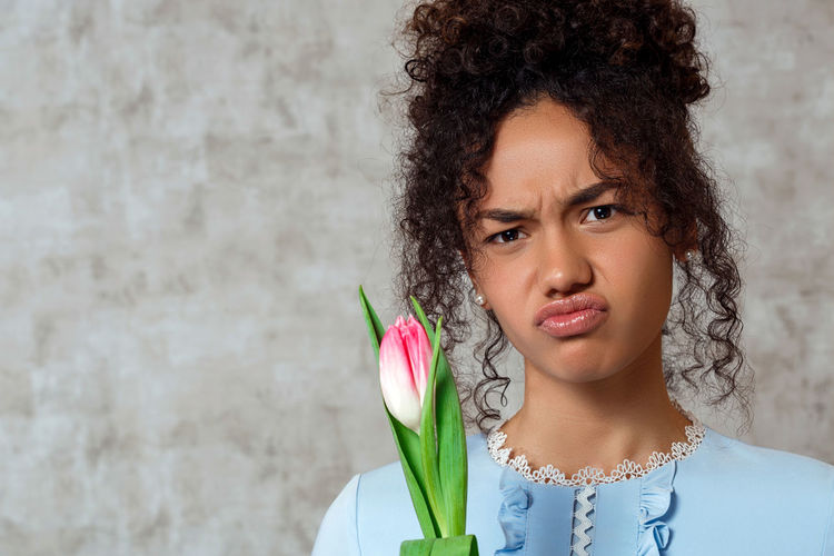 Portrait of young woman with tulip making a face while standing against wall