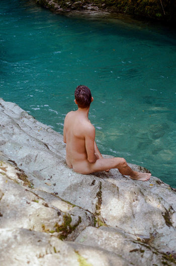 Rear view of shirtless man sitting on rock