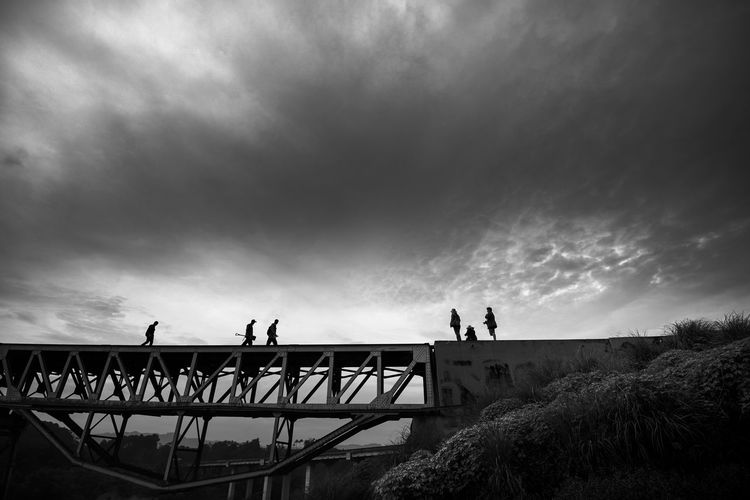 Silhouette people standing on bridge against sky