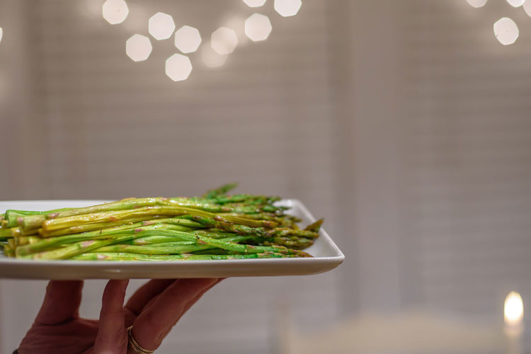 Closeup of hand holding up a plate of fresh steamed asparagus 