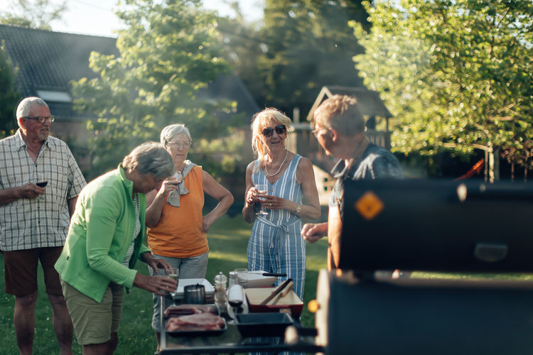 Group of senior people enjoying life on a barbecue in the garden - elderly friends talk and drink 
