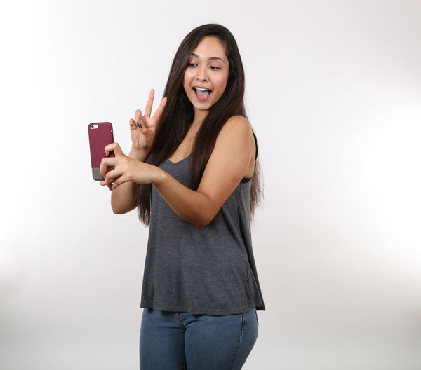 Smiling young woman using phone while standing against white background