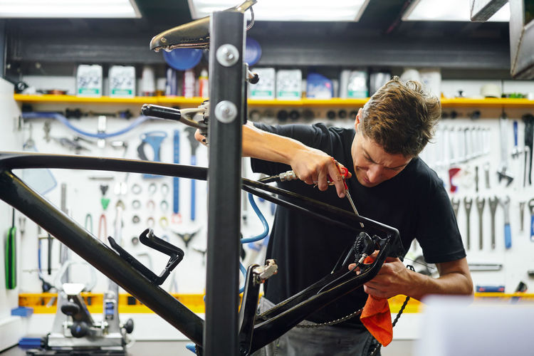 Focused male master wiping bike frame with rag while working in modern repair workshop