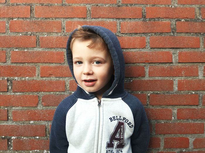 Portrait of cute boy standing against brick wall