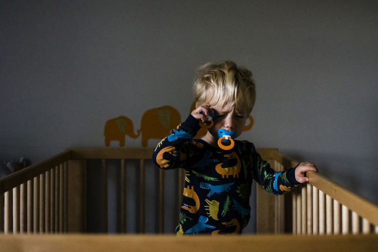 Boy with pacifiers standing in crib