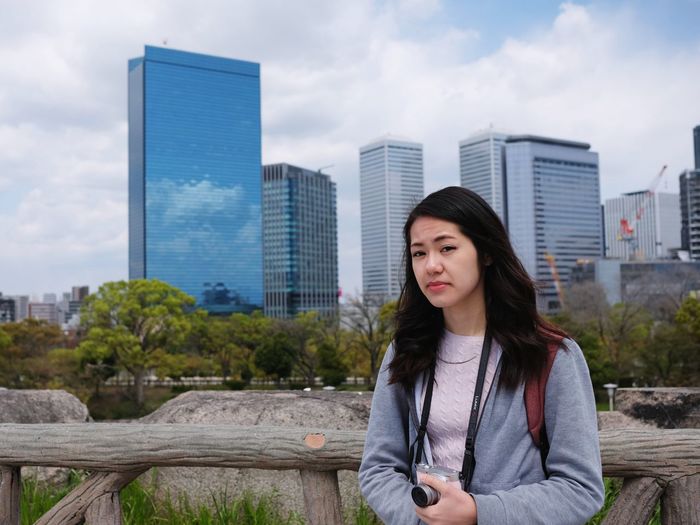 Beautiful young woman standing against sky in city