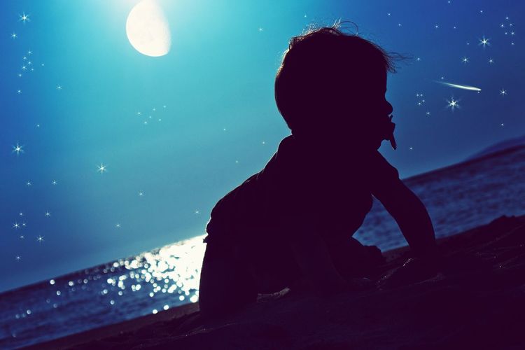 Silhouette toddler on sea shore against sky