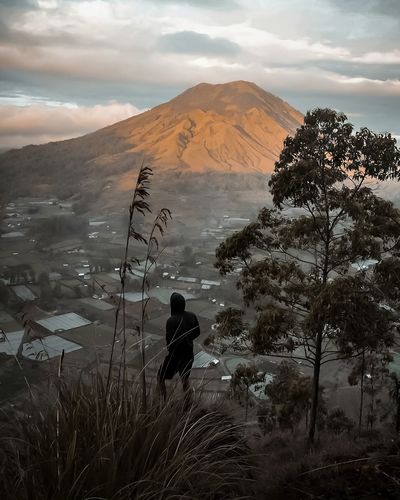 Rear view of man looking at houses and mountain against cloudy sky