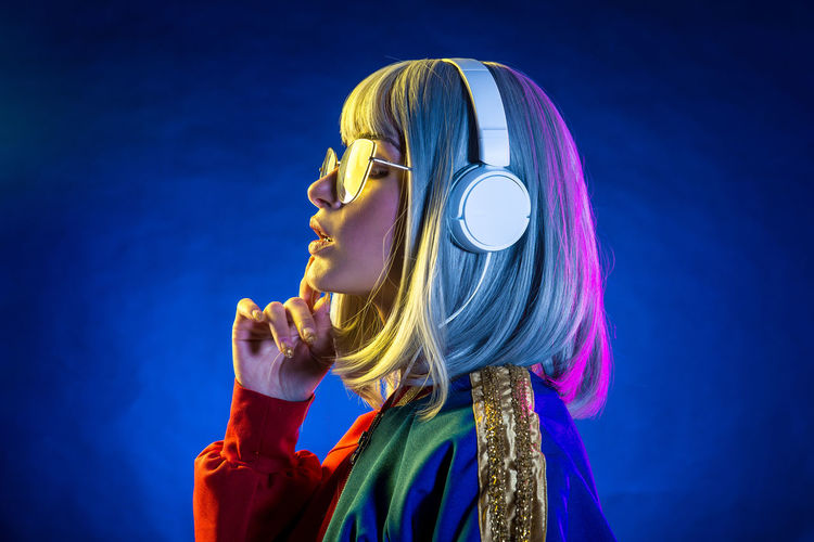 Side view of woman wearing headphones against blue background