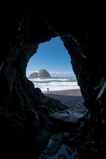 Person at beach against sky seen through cave