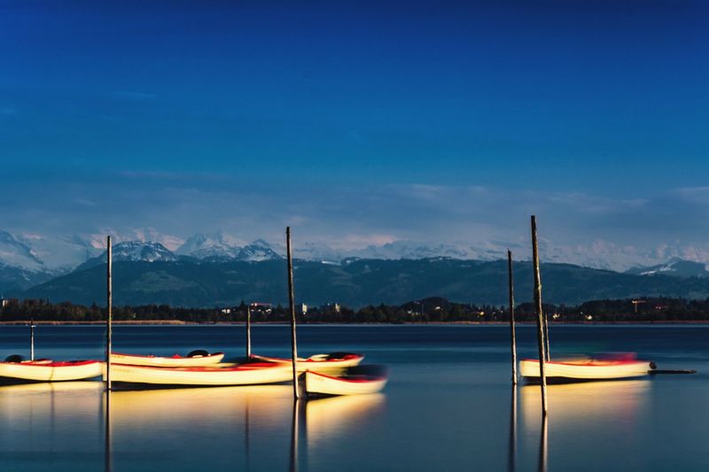 Fishing boats anchored on river against snowcapped mountains