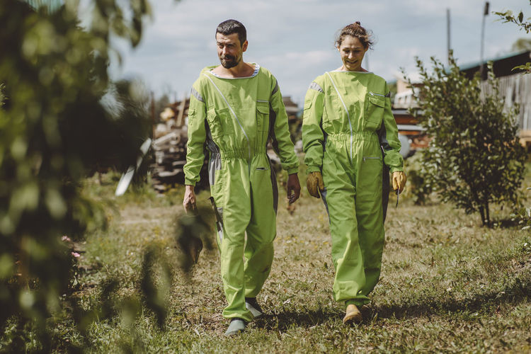 Happy beekeepers wearing protective suits walking together on apiary