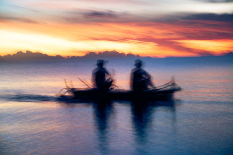 Silhouette people sailing on sea against sky during sunset