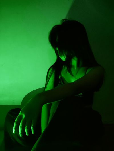 Side view of woman sitting on floor at home with greenlights on