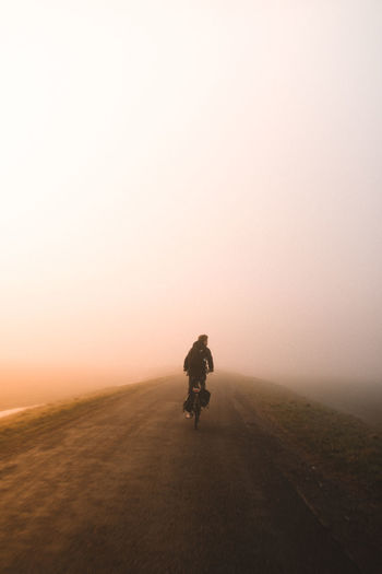 Rear view of man cycling on road during foggy weather
