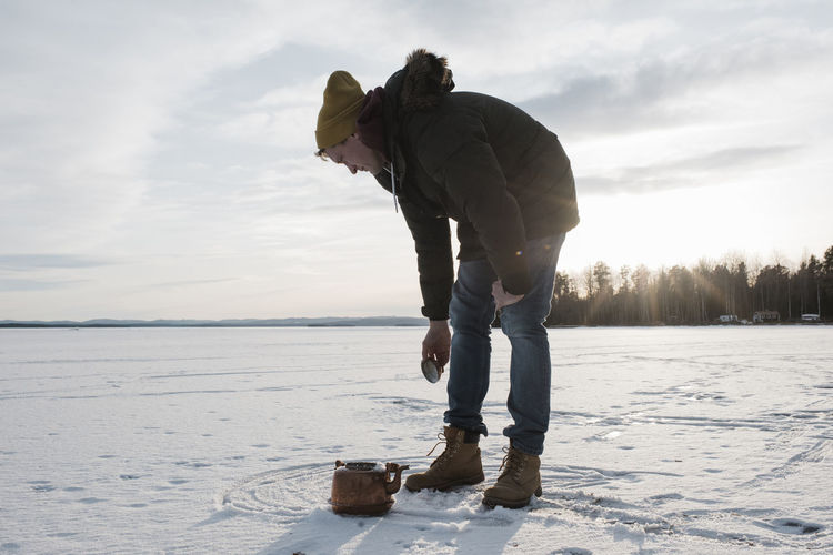 Man collecting snow to boil in a kettle on a camp fire whilst camping