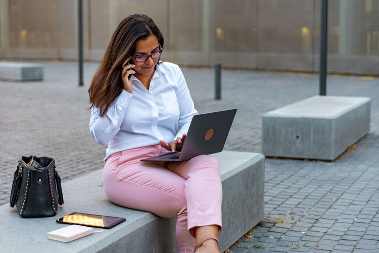 Young woman using mobile phone while sitting in laptop