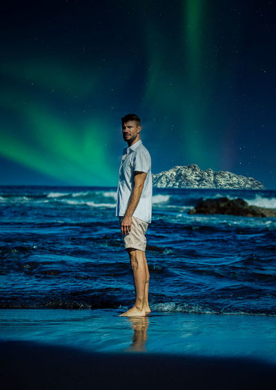 Young man standing in sea against sky at night