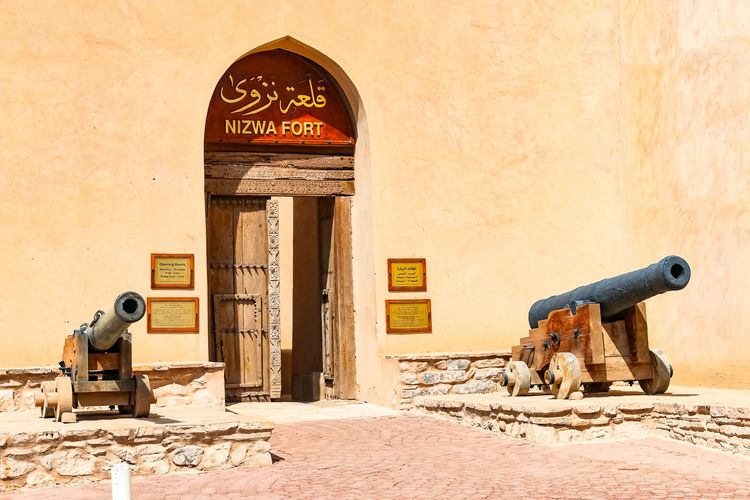 The facade of the fortress of nizwa with wooden door and cannons, nizwa, oman