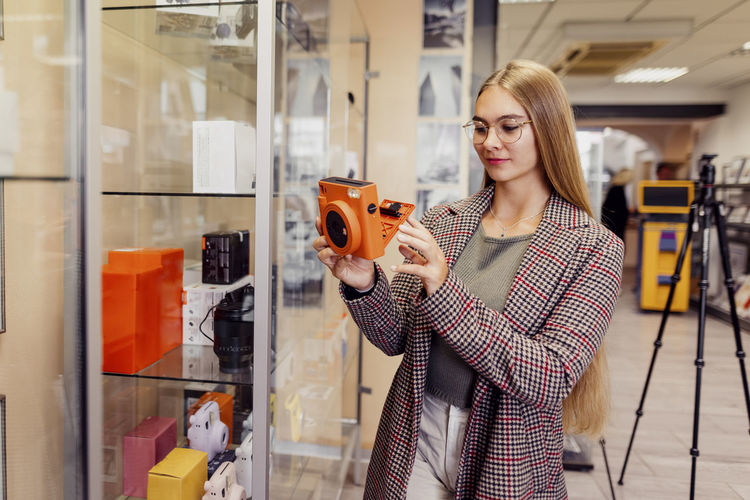 Young woman examining instant camera in shop