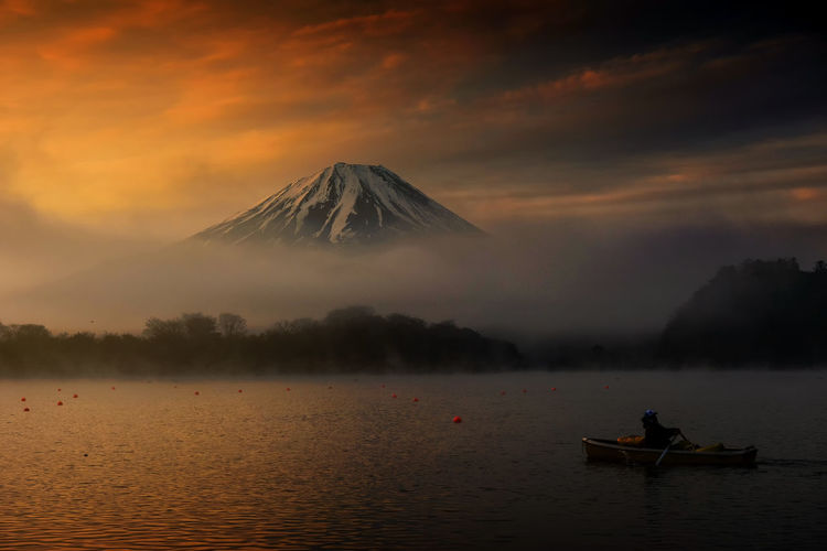 Silhouette man on lake by mountains against sky during sunset
