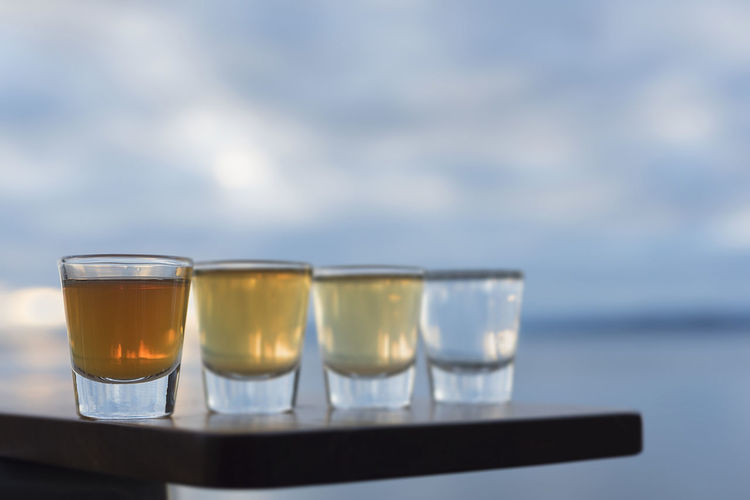 Tequila shots on table by sea against sky