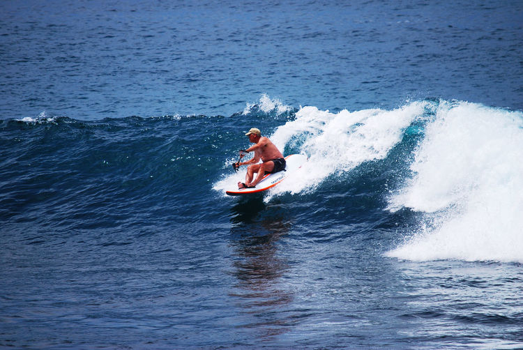 Full length of shirtless man surfing in boat on sea