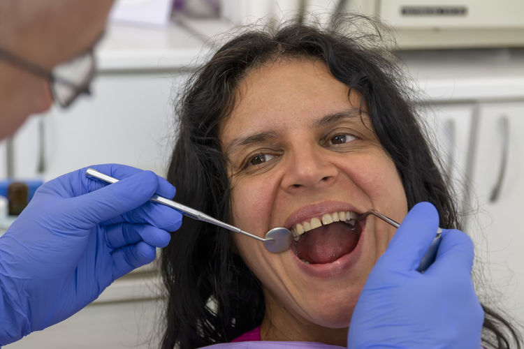 A middle-aged woman sitting in medical chair while dentist fixing her teeth at dental clinic