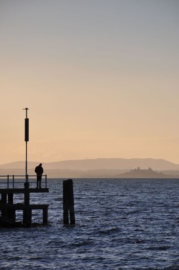 Silhouette man on sea against clear sky during sunset