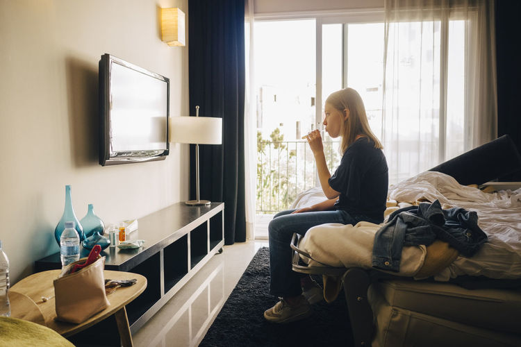 Side view of girl watching television while sitting on bed in hotel room