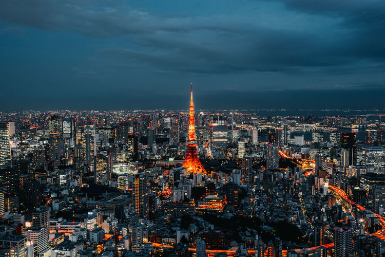Aerial view of illuminated tokyo tower amidst buildings against cloudy sky in city at night