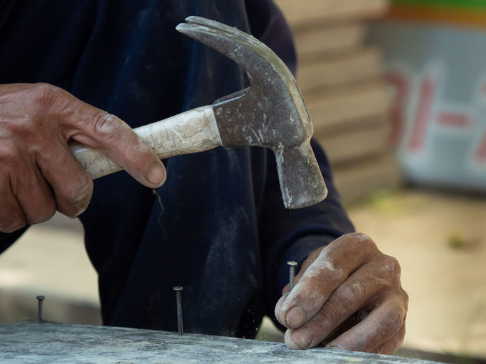 Midsection of man hammering nail on plank