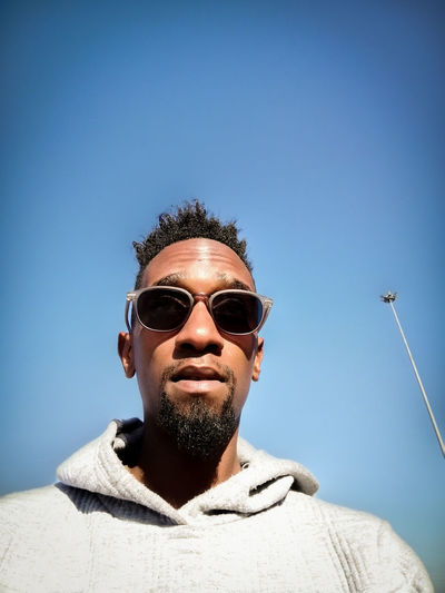 Portrait of man wearing sunglasses against clear blue sky